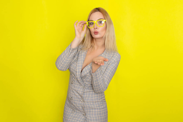 Attractive blonde woman in plaid jacket dress over yellow background wearing yellow glasses - Photo, Image