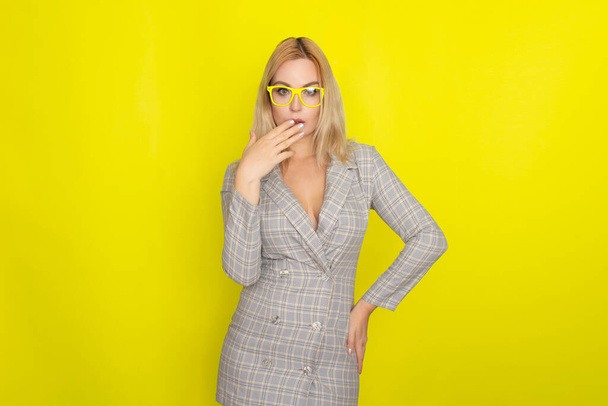 Attractive blonde woman in plaid jacket dress over yellow background wearing yellow glasses - Φωτογραφία, εικόνα