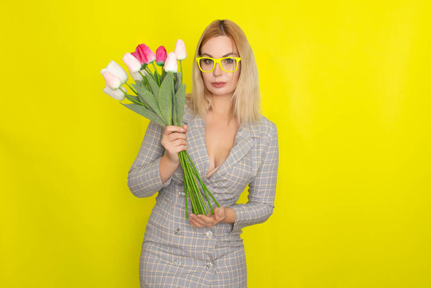 Blonde woman in plaid dress holding tulips bouquet over yellow background - Foto, Bild