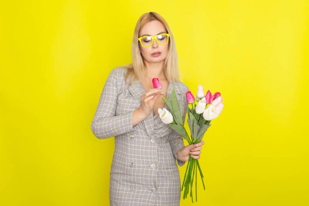 Blonde woman in plaid dress holding tulips bouquet over yellow background - Fotografie, Obrázek