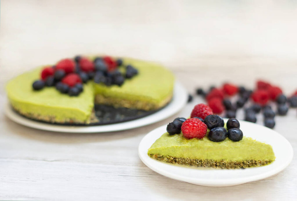 Lekkere zelfgemaakte avocado en limoen Rauwe cake met bosbessen en frambozen, gezonde veganistische recepten - Foto, afbeelding