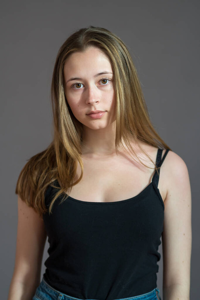 Πορτρέτο ενός ελκυστικού έφηβου κοριτσιού φορώντας ένα καμισόλ που ποζάρει κοιτάζοντας την κάμερα σε γκρι φόντο - Φωτογραφία, εικόνα