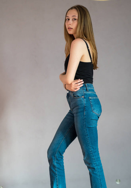 Lichaamsportret van een mooi tienermeisje met een zwart topje en spijkerbroek op de camera. Studioshoot - Foto, afbeelding