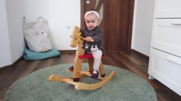 Felice bambina che gioca su un cavallo a dondolo in legno. Infanzia, gioco a casa concetto - Filmati, video