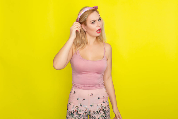 Blonde woman in pink summer clothing wearing pink headphones like kitten ears - Valokuva, kuva