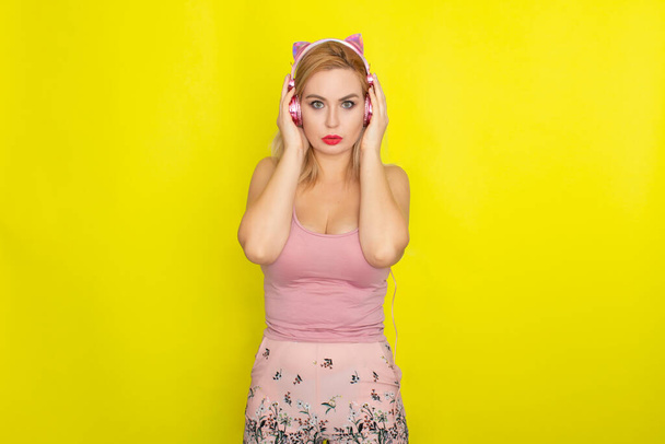 Blonde woman in pink summer clothing wearing pink headphones like kitten ears - Foto, Bild