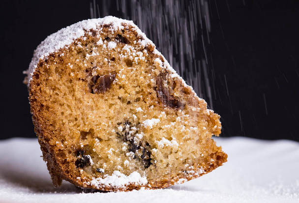 Ripottelemalla tuhkeria jauhe päälle pala tuoretta makea muffinssi kakku rusinoita lähikuva mustalla pohjalla. - Valokuva, kuva