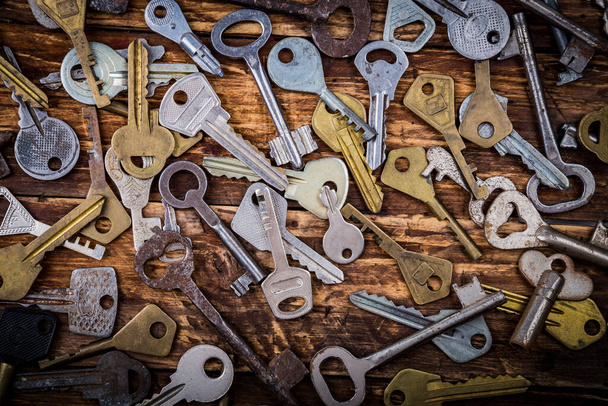 Muchas llaves antiguas de metal multicolor variadas de diferentes formas en el fondo de la mesa rayada de madera. Concepto de seguridad doméstica
. - Foto, Imagen