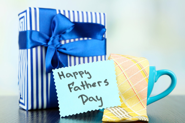 Happy Fathers Day tag with gift boxes, cup and tie, on wooden table, on light background - Photo, image