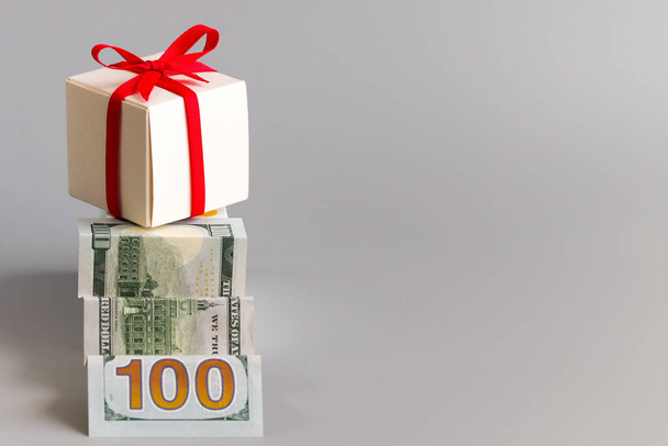 A hundred dollars folded like a ladder and a gift box tied with red ribbon. The concept of hoarding, wealth and surprises. Free space for text - Photo, Image