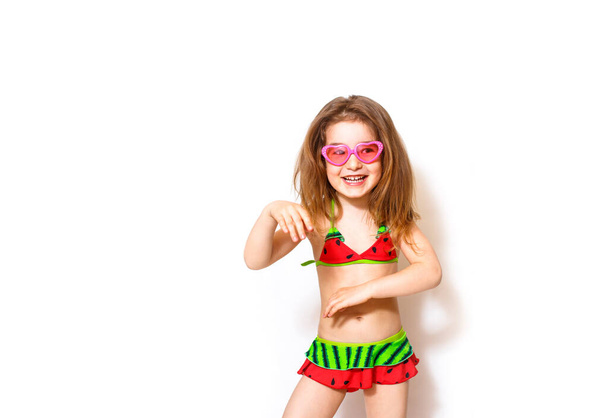 A little  happy girl in a beach outfit, bathing suit, yellow straw hat, pink heart-shaped sunglasses. Ready for a beach holiday, sun protection, children's fashion. White background, space for text.  - Photo, image