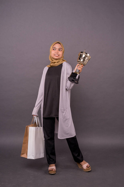 Clever Consumer concept.Happy malay girl holding shopping bags and Gold trophy. - Foto, imagen