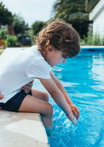 Pieni iloinen poika istuu puolella uima-allas puutarhassa hauskaa. Kesällä. Kesälomat. - Valokuva, kuva