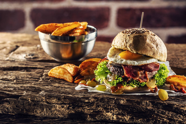 Beef burger with fried egg, bacon, lettuce, potato wedges and grapes on a rustic wood - Valokuva, kuva