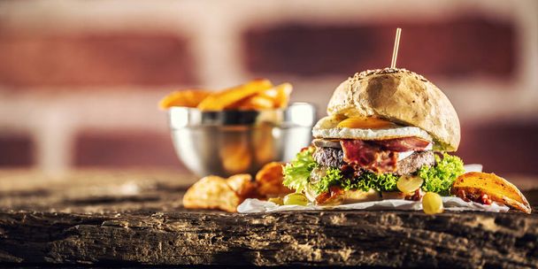 Beef Burger mit Spiegelei, Speck, Salat, Kartoffelkeilen und Trauben auf rustikalem Holz - Foto, Bild