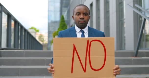 Retrato de ativista afro-americano em terno e gravata segurando cartaz Não em demonstração. Um protesto ao ar livre. Conceito de negação do ativismo. Homem mostrando mesa com palavra não. Declaração de recusa
. - Filmagem, Vídeo