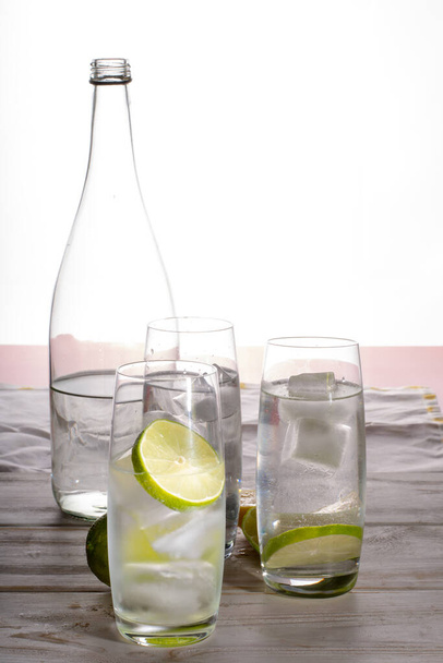 Stil mineral drink water in glass bottle served with three glasses with ice cubed, lime and lemon - Фото, изображение