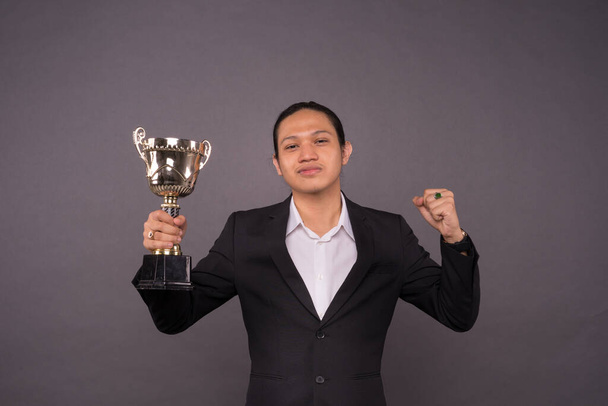 A young business man holding a gold trophy and celebrate his archivement. - Photo, Image