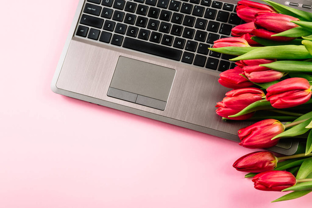 ノートパソコンとチューリップの花の花束とオフィスデスクテーブル。コピースペース付きのトップビュー - 写真・画像