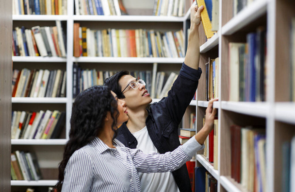 Uśmiechnięci licealiści czytający książki w bibliotece - Zdjęcie, obraz