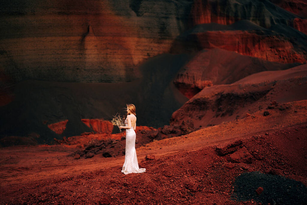 Porträt einer Braut Modell in einem goldenen Brautkleid, in einem gelb-roten Sandbruch, im Krater eines Vulkans in Island, Golden Circle. Strauß von Haken und goldenen Zweigen. - Foto, Bild