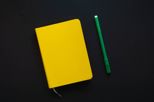 A yellow pad and a green pen on a black background. Top view. - Фото, изображение