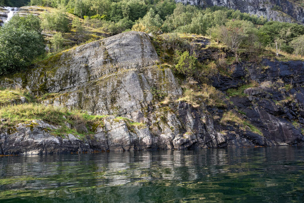 Βαριά γκρίζα βράχια με πράσινο γρασίδι και αντανάκλαση του νερού, νορβηγικό φιόρδ Aurlandsfjord. Φωτεινή θέα στα άγρια βουνά, τη φύση της Νορβηγίας. Καγιάκ Σκανδιναβία - Φωτογραφία, εικόνα