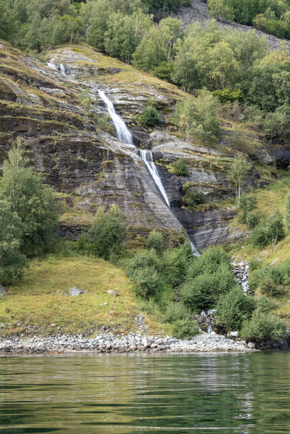 Wasserfall fällt, norwegischer Fjord Aurlandsfjord Wasserspiegel Reflexion. Heller vertikaler Blick auf die wilde Bergnatur Norwegens. Sonniger Reisetag. - Foto, Bild