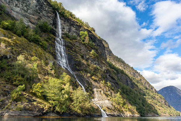 Wodospad wpadający w norweski fiord Aurlandsfjord. Zamknij jasny widok na białą wodę na dzikie góry przyrody Norwegii. Słoneczny dzień podróży. - Zdjęcie, obraz