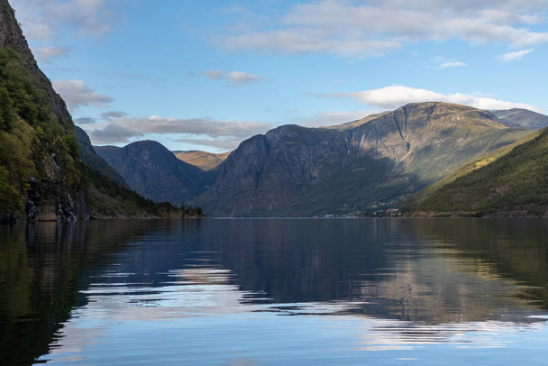 Kilátás vízfelszínről fényes tükröződéssel. Norvégia Aurlandsfjord fjord utazás, kajakozás túra. Természet, hegyek, kék táj, felhős epikus kilátás. - Fotó, kép