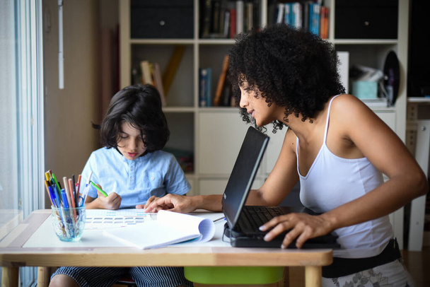 metis vrouw in telewerken thuis terwijl haar zoon doet zijn huiswerk - Foto, afbeelding
