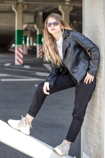 young blonde schoolgirl in black leather jacket posing in the parking lot - Zdjęcie, obraz
