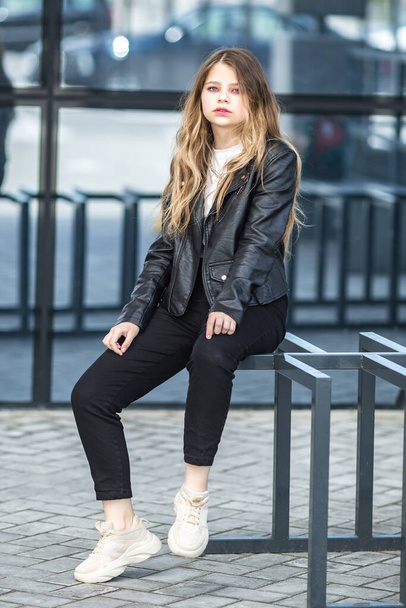 young blonde schoolgirl in black leather jacket posing in the parking lot - Foto, Imagen