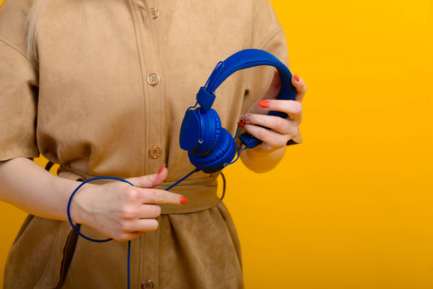 Young woman with blue headphones in hands on yellow background - Foto, Imagen