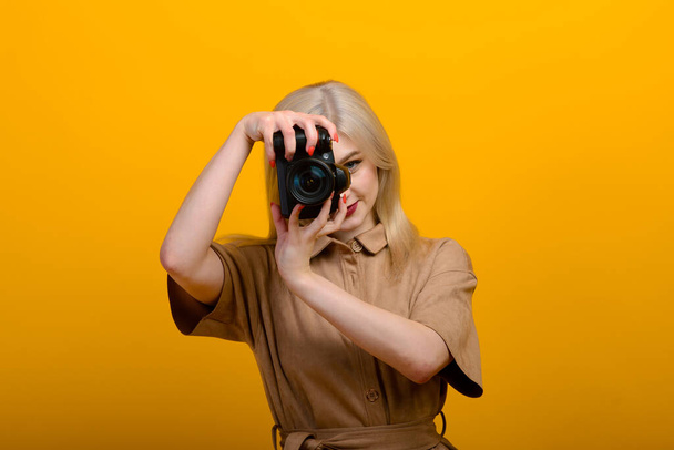 Muotokuva vaaleasta tytöstä, jolla on kamera kädessään keltaisella taustalla. Eristetty studio
. - Valokuva, kuva