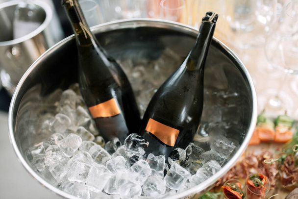 Deux bouteilles de champagne sont refroidies dans un vase avec de la glace. - Photo, image