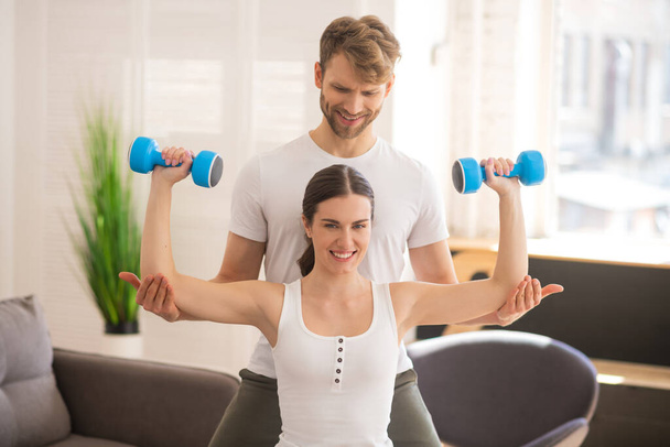 Smiling woman working on her muscles and her husband helping her - Фото, изображение