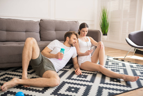Young couple sitting on the floor after a home workout and making photos - Φωτογραφία, εικόνα