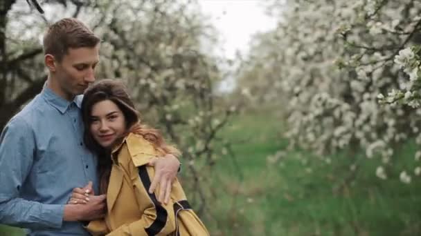 Glücklich verliebtes junges Paar bei einem Spaziergang im frühlingshaft blühenden Garten. Der Kerl umarmt das Mädchen und sie schauen sich an. Nahaufnahme. Zeitlupe - Filmmaterial, Video