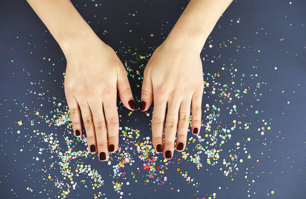 Top view of crop anonymous female with bright manicure over dark blurred background with colorful confetti - Foto, immagini