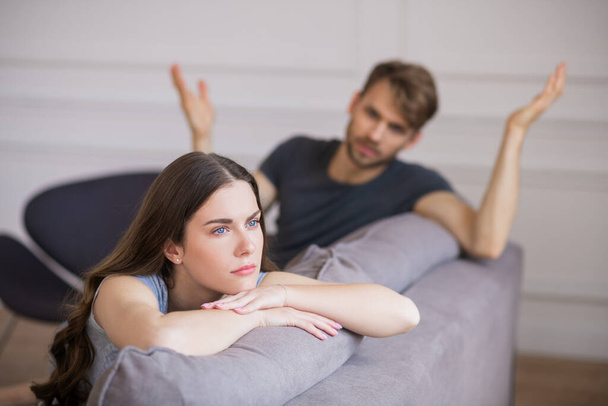 Young woman sitting with a depressed look while her husband blaming her - Foto, Bild