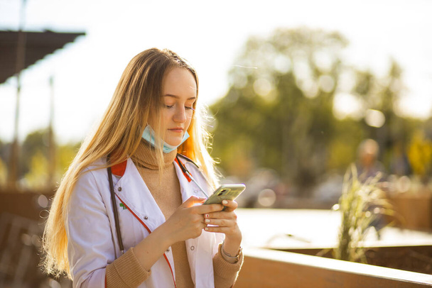 Female doctor or nurse uses smartphone during break - Foto, afbeelding