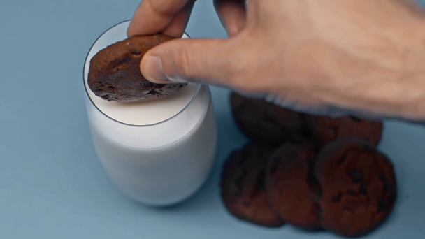Langzame beweging van mens dompelkoekje in glas melk op blauw oppervlak - Video