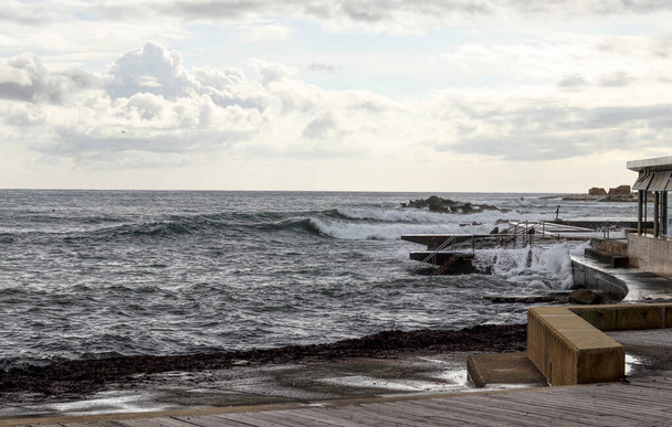 Άποψη της κυπριακής ακτής κοντά στην Πάφο και της φουρτουνιασμένης θάλασσας που κορυφώνεται από έναν όμορφο ουρανό όπου ένα μαύρο σύννεφο εναλλάσσεται με μπλε. Θάλασσα που χορεύει. Κάθε σκιά του μπλε. Πάφος, Κύπρος, Νότια Ευρώπη. - Φωτογραφία, εικόνα