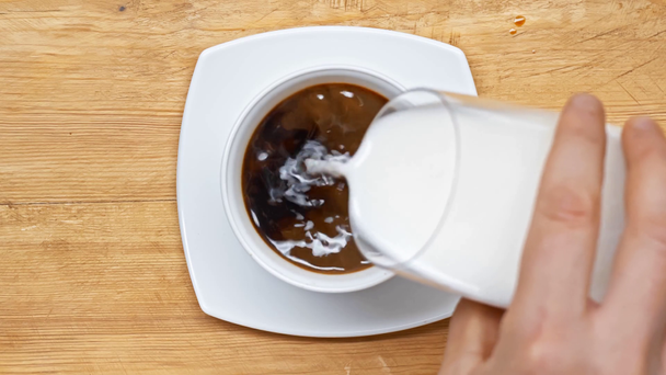 Widok z góry człowieka wylewanie mleka w kawie na drewnianej powierzchni - Materiał filmowy, wideo