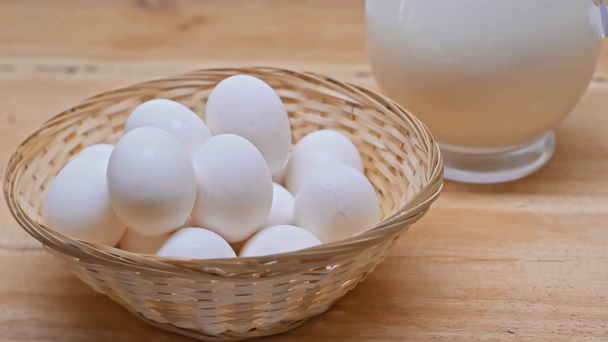 Αργή κίνηση του ανθρώπου λαμβάνοντας αυγό από το καλάθι κοντά κανάτα γάλα σε ξύλινη επιφάνεια - Πλάνα, βίντεο