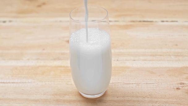 Milk pouring in glass on wooden surface - Video, Çekim