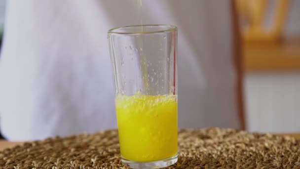 Mujer vertiendo limonada naranja en vidrio. Cierre del llenado de vidrio transparente con sosa en la cocina. - Imágenes, Vídeo