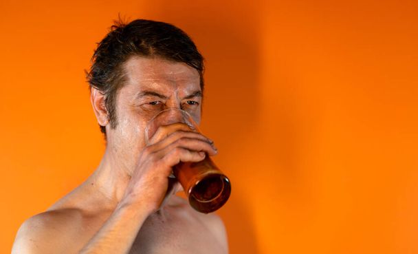 Дорослий чоловік з голим торсом п'є пиво зі склянки. Поняття: алкоголізм і алкоголізм
 - Фото, зображення