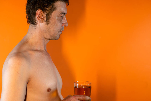 An adult male with a naked torso drinks beer from a glass glass. Concept: Alcoholism and the alcoholic man - Foto, Bild